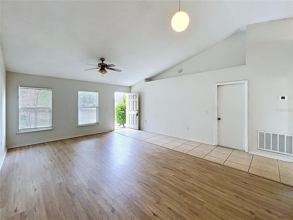 An empty living room features wood-look flooring, a vaulted ceiling, and a tiled entryway — 6004 KALEY DRIVE, WINTER HAVEN, FL