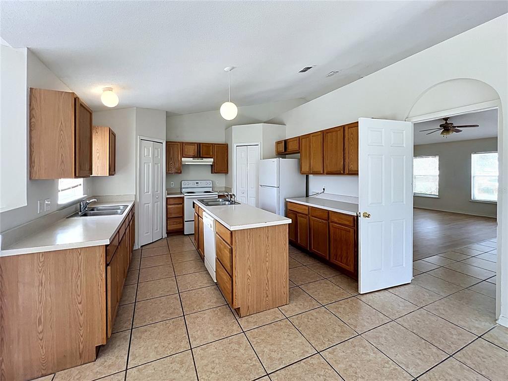 A kitchen with wood cabinets, white appliances, an island, and tile flooring — 6004 KALEY DRIVE, WINTER HAVEN, FL