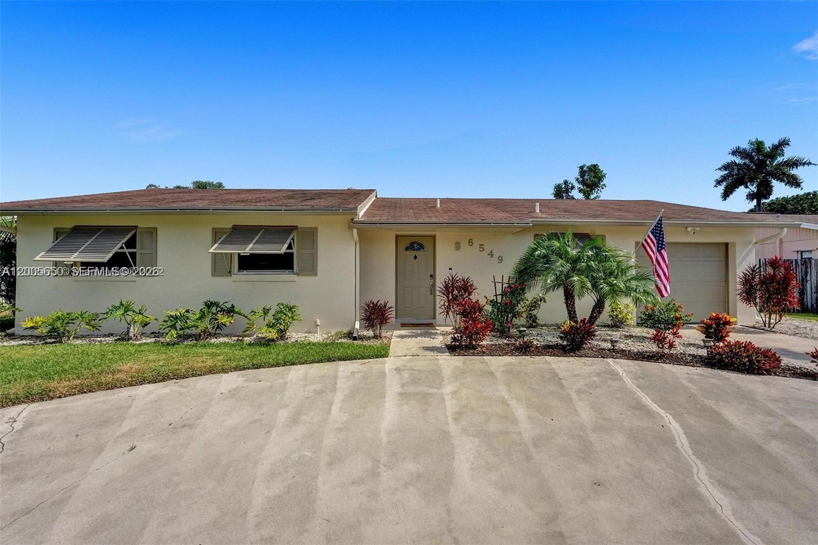 A single-story house with a concrete driveway, beige exterior, and an American flag — 6549 Sleepy Willow Way # 6549, Delray Beach FL 33484, DELRAY BEACH, FL