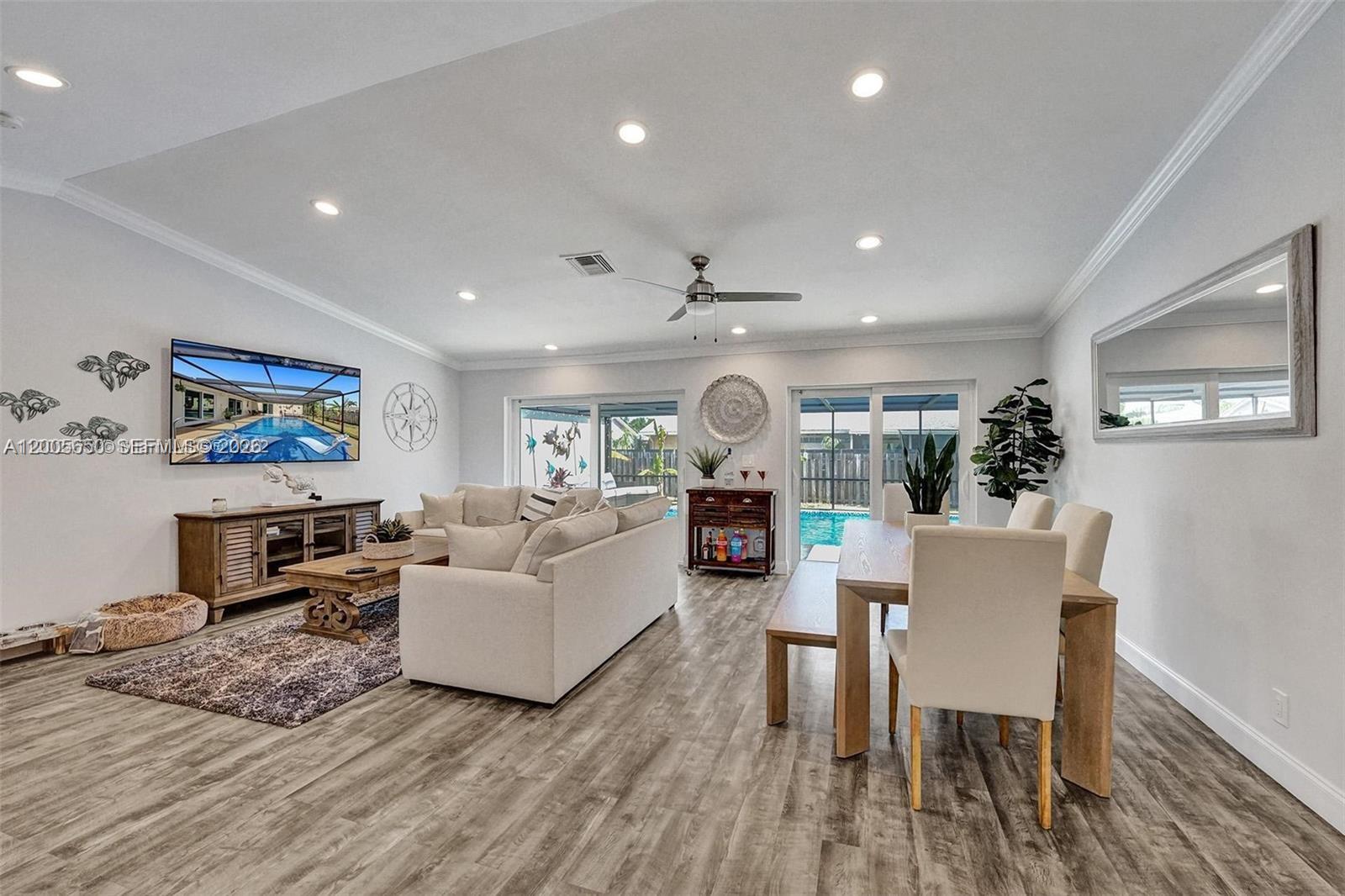 An open-concept living and dining area features light wood-look flooring and views of a pool — 6549 Sleepy Willow Way # 6549, Delray Beach FL 33484, DELRAY BEACH, FL
