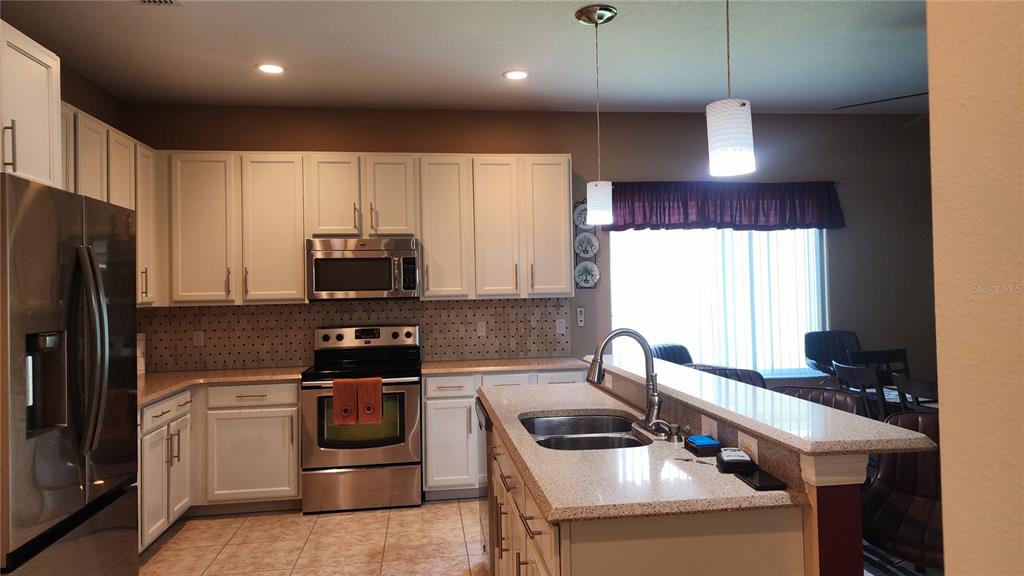 A kitchen features white cabinets, stainless steel appliances, a granite island, and tile flooring — 1915 ACACIA DRIVE, KISSIMMEE, FL