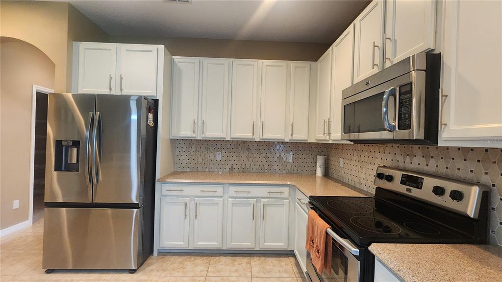 A kitchen features white cabinets, stainless steel appliances, a patterned backsplash, and tan countertops — 1915 ACACIA DRIVE, KISSIMMEE, FL