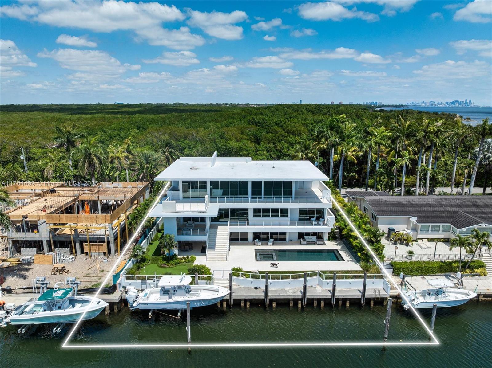 An aerial view of a three-story modern waterfront home with a pool and docked boats — 830 Lugo Ave, Coral Gables FL 33156, CORAL GABLES, FL