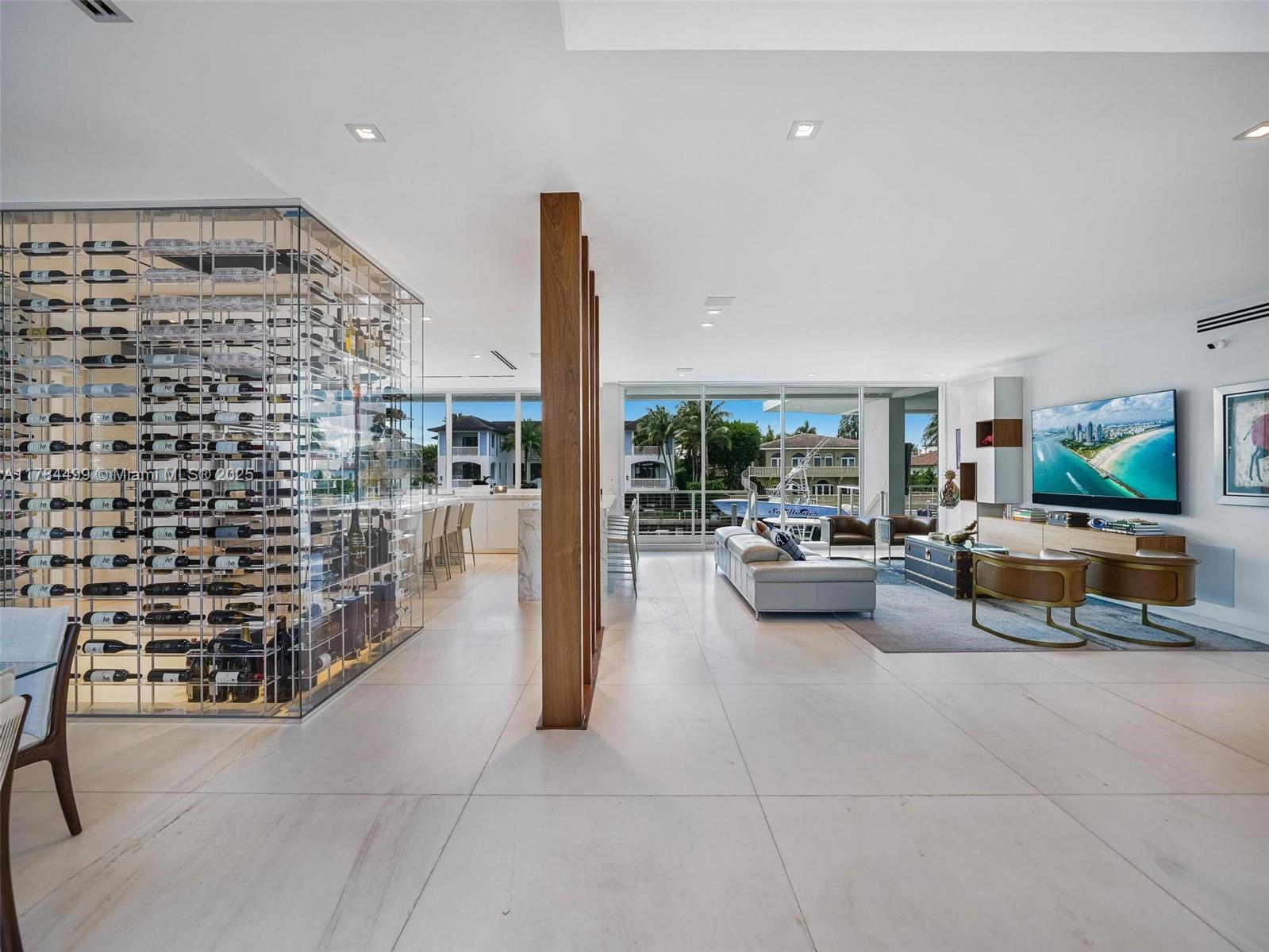 A modern living room features a glass-enclosed wine cellar, light tile floors, and waterfront views — 830 Lugo Ave, Coral Gables FL 33156, CORAL GABLES, FL