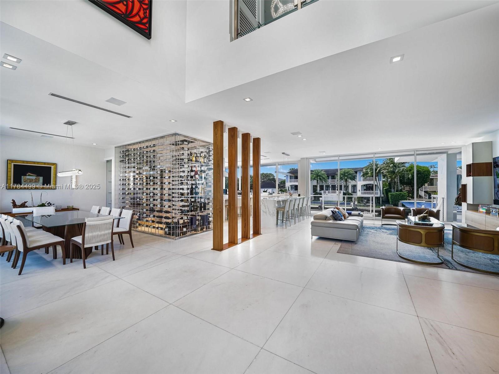 A modern open-concept living and dining area features a glass wine cellar and floor-to-ceiling windows — 830 Lugo Ave, Coral Gables FL 33156, CORAL GABLES, FL