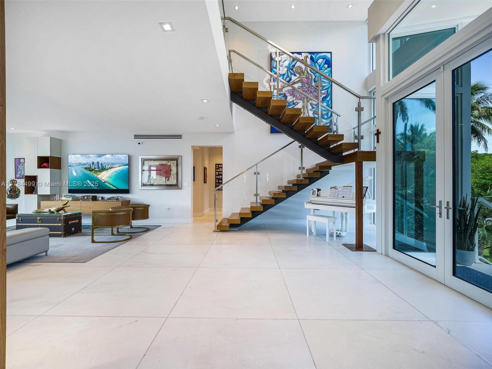 A modern living room features white tile floors, a floating staircase, and a white piano — 830 Lugo Ave, Coral Gables FL 33156, CORAL GABLES, FL