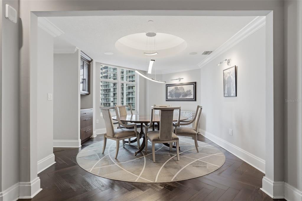 A modern foyer with a glass-railed staircase, herringbone wood floors, and a large chandelier — 100 BEACH DRIVE NE UNIT 1900, ST PETERSBURG, FL