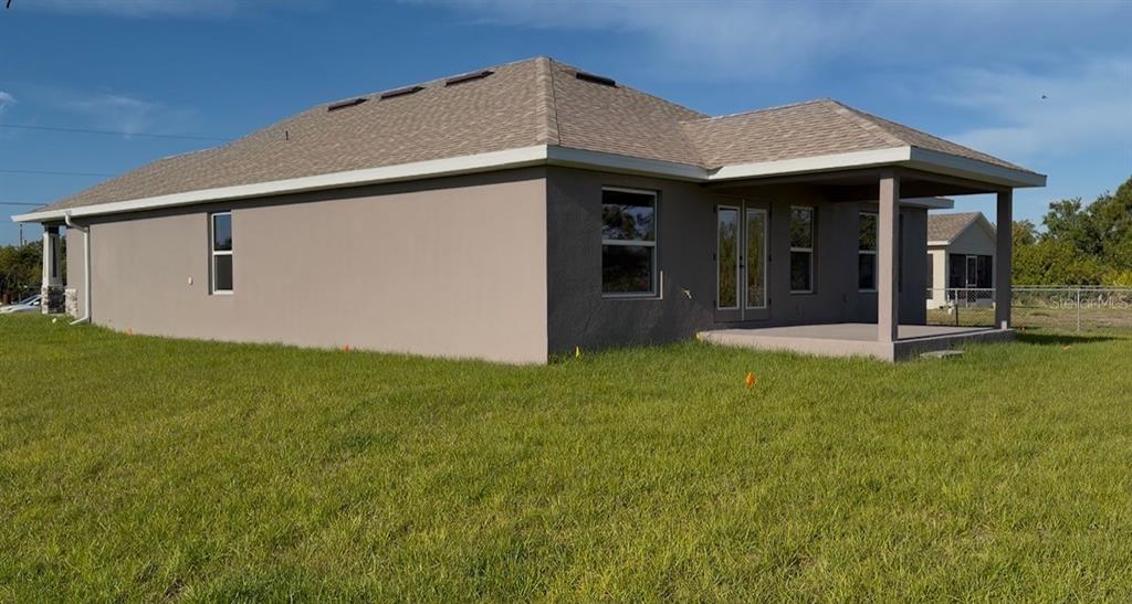 The exterior rear view of a tan stucco house with a covered patio and lawn — 12152 DUBARRY AVENUE, PORT CHARLOTTE, FL