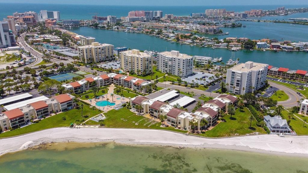 An aerial view shows a beachfront condominium complex with a pool and surrounding coastal buildings — 865 S GULFVIEW BOULEVARD UNIT 207, CLEARWATER BEACH, FL