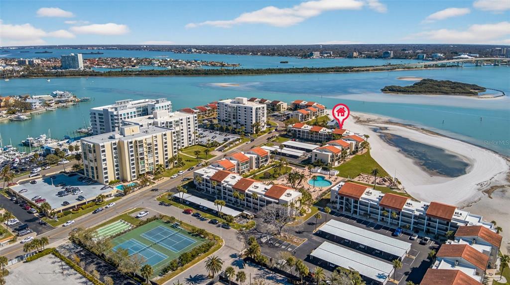 An aerial view shows a coastal condominium complex with a pool, tennis courts, and beach — 865 S GULFVIEW BOULEVARD UNIT 207, CLEARWATER BEACH, FL