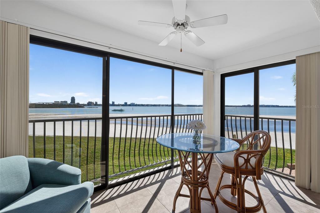 A sunroom with a glass table, wicker chairs, and sliding doors overlooking a waterfront view — 865 S GULFVIEW BOULEVARD UNIT 207, CLEARWATER BEACH, FL