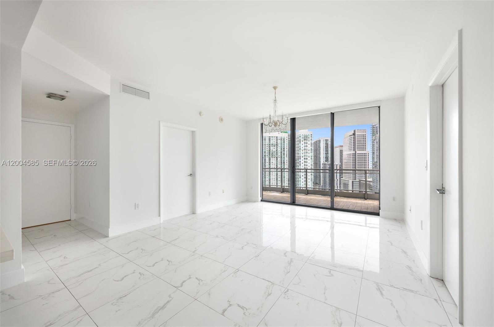 A bright, empty room features white marble-look tile floors, a chandelier, and a balcony view — 90 SW 3rd St # 2602, Miami FL 33130, MIAMI, FL
