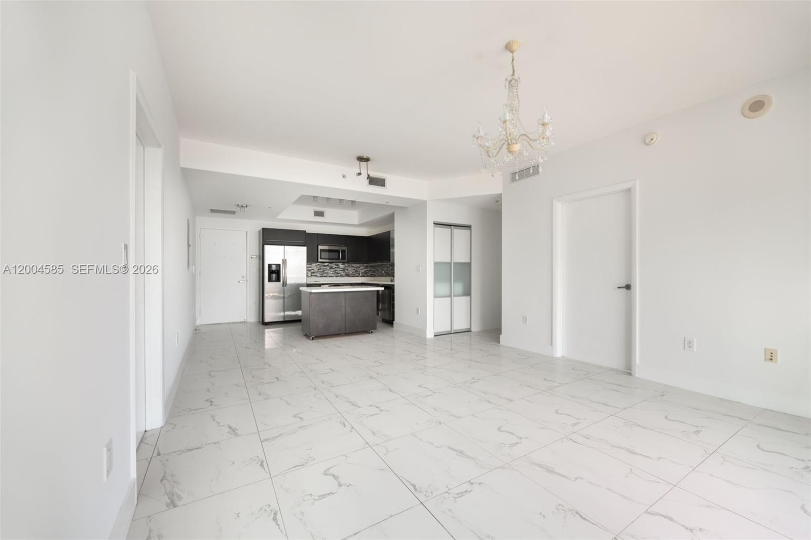An open-concept room features white marble-look tile flooring, a kitchen island, and a crystal chandelier — 90 SW 3rd St # 2602, Miami FL 33130, MIAMI, FL