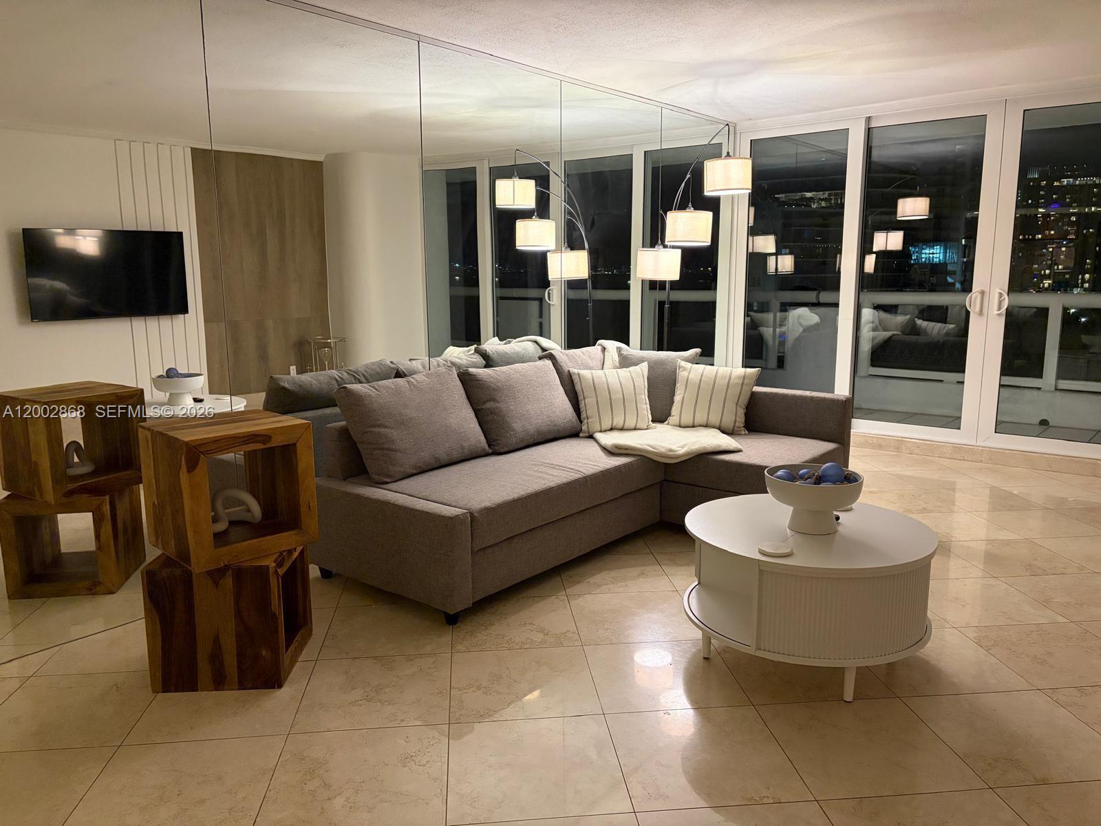 A living room features a gray sectional sofa, a white coffee table, and mirrored walls — 1717 N Bayshore Dr # 1236, Miami FL 33132, MIAMI, FL