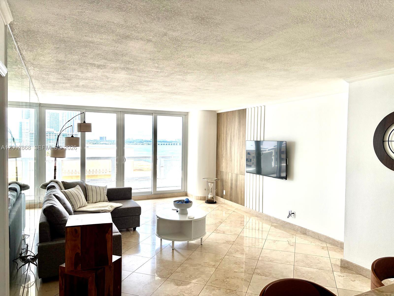 A living room features tile floors, a gray sectional sofa, and a wall-mounted television — 1717 N Bayshore Dr # 1236, Miami FL 33132, MIAMI, FL