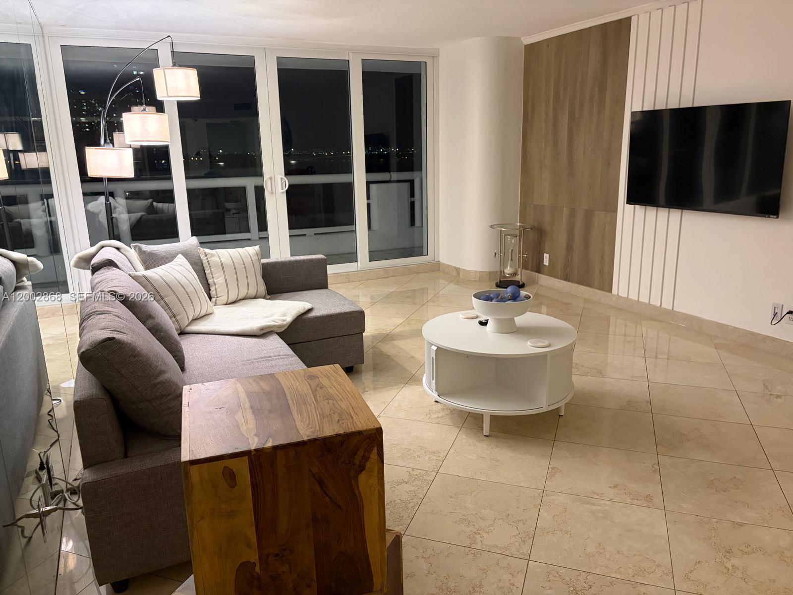 A living room features a grey sectional sofa, a round white coffee table, and tile flooring — 1717 N Bayshore Dr # 1236, Miami FL 33132, MIAMI, FL