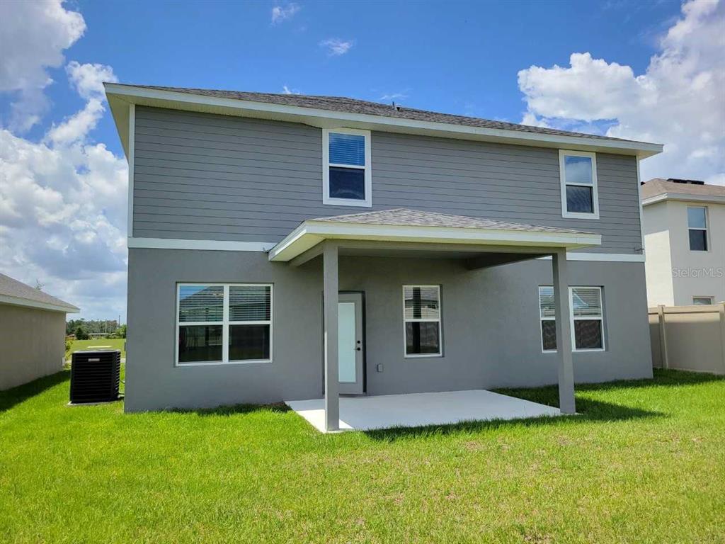 The back exterior of a two-story house features gray siding, a covered patio, and grass — 4380 SW 92ND PLACE ROAD, OCALA, FL