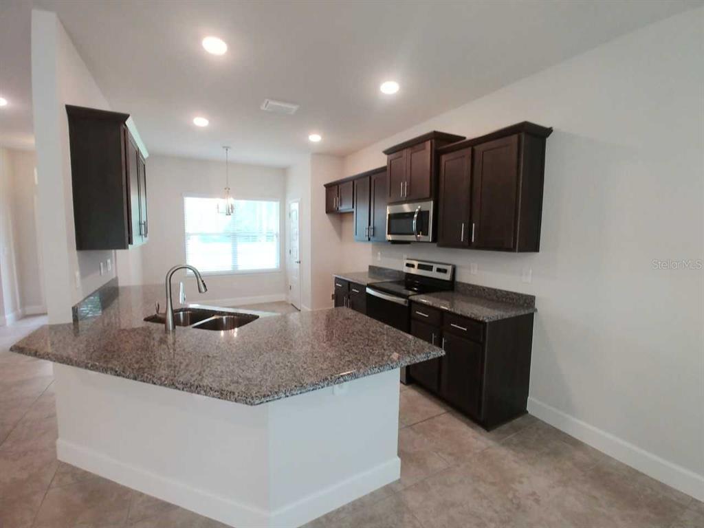 A kitchen features dark wood cabinets, granite countertops, and a breakfast bar island — 4380 SW 92ND PLACE ROAD, OCALA, FL