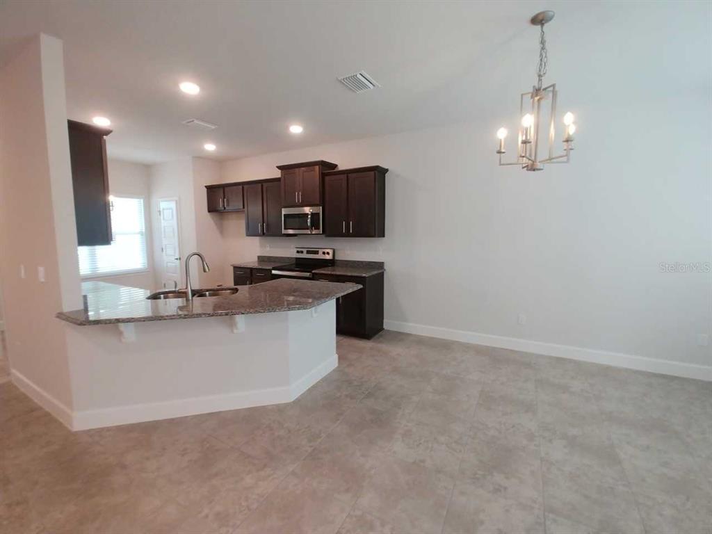 A kitchen with dark cabinets, granite countertops, and a breakfast bar opens to a dining area — 4380 SW 92ND PLACE ROAD, OCALA, FL