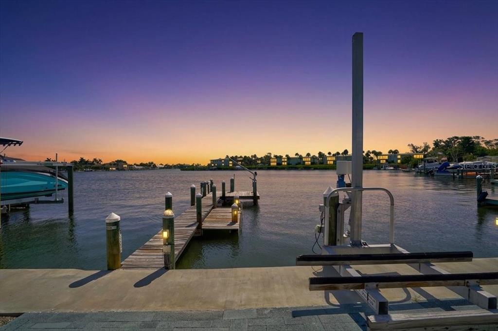 A wooden boat dock extends into a calm waterway at sunset with a boat lift nearby — 17 SEASIDE COURT, HOLMES BEACH, FL
