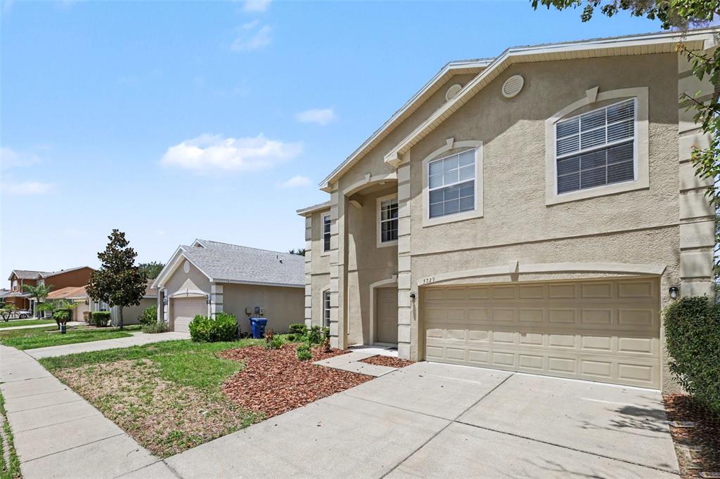 A two-story beige stucco house with a two-car garage and a concrete driveway — 5729 SWEET WILLIAM TERRACE, LAND O LAKES, FL