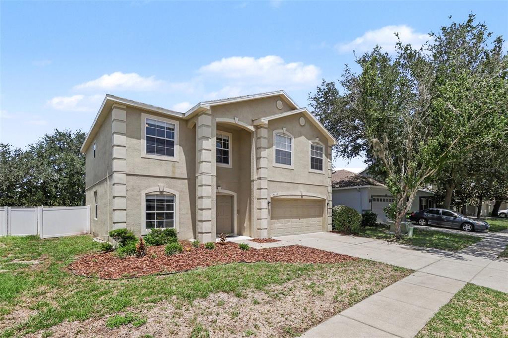 A two-story tan stucco house with a two-car garage and a front lawn — 5729 SWEET WILLIAM TERRACE, LAND O LAKES, FL