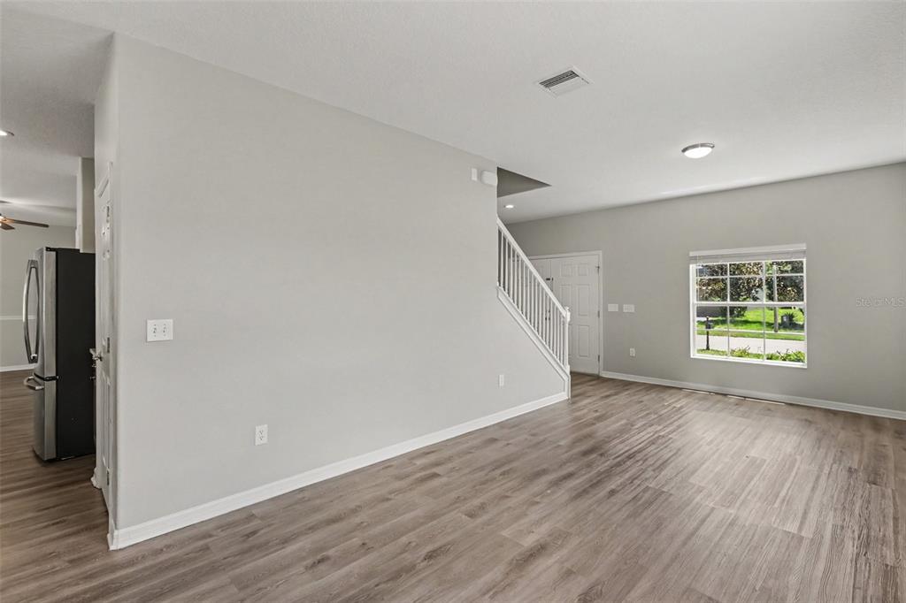 An open living area features light gray walls, wood-look flooring, and a staircase with railings — 5729 SWEET WILLIAM TERRACE, LAND O LAKES, FL