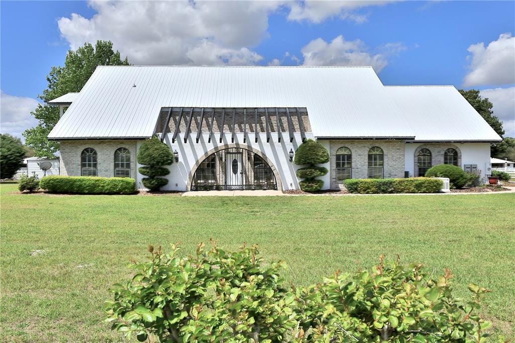 A single-story house with a white metal roof, brick exterior, and a central arched entryway — 4450 SE 216TH AVENUE, MORRISTON, FL