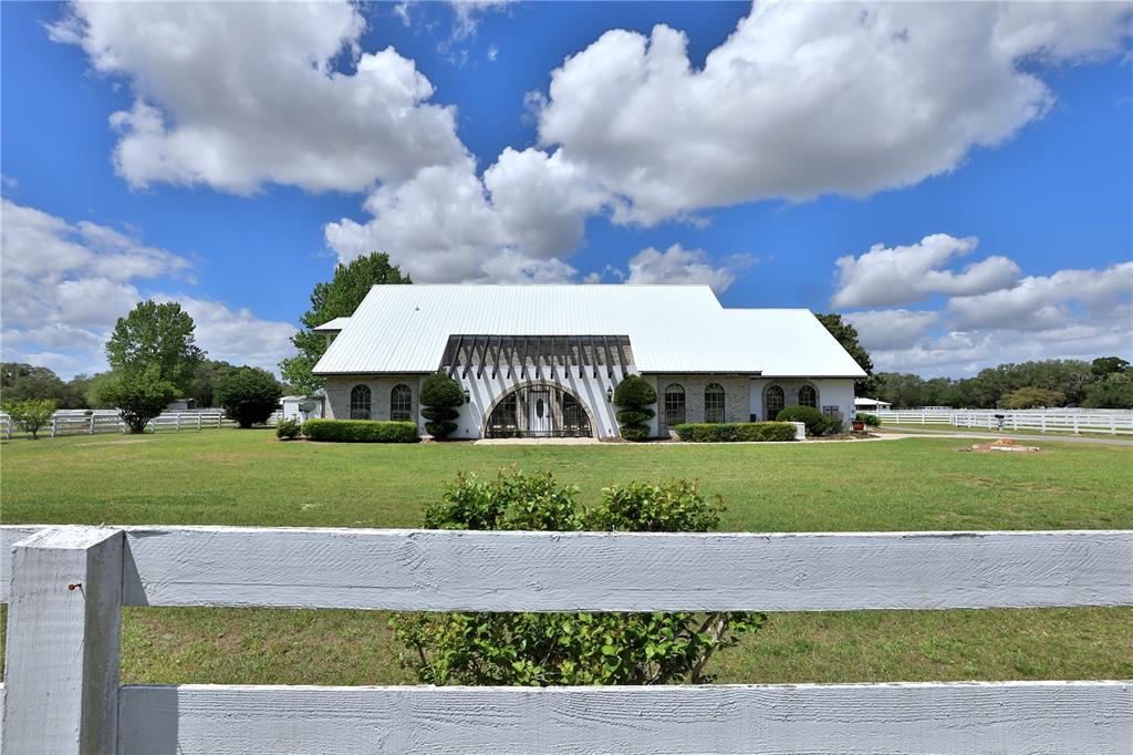 A white house with a metal roof and a large arched entryway sits on grass — 4450 SE 216TH AVENUE, MORRISTON, FL