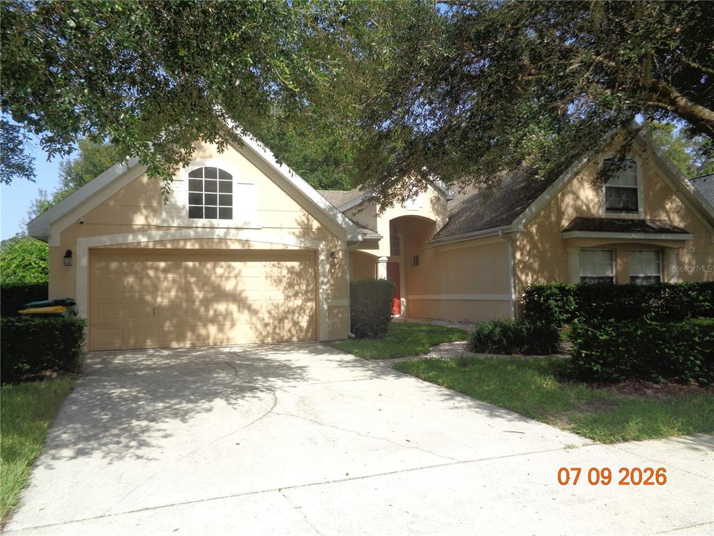 A tan, single-story suburban house features a two-car garage and a concrete driveway — 1409 BENT OAKS BOULEVARD, DELAND, FL