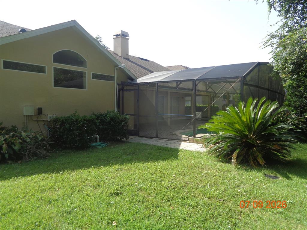 A yellow house features a screened-in pool enclosure and a grassy backyard — 1409 BENT OAKS BOULEVARD, DELAND, FL
