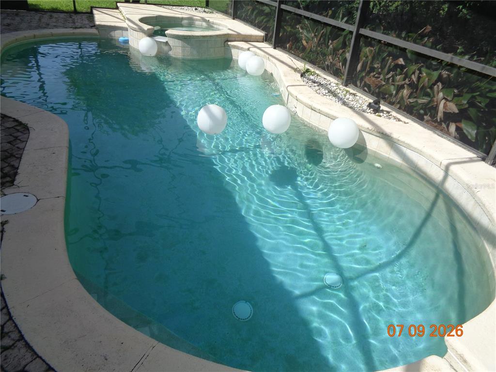 A swimming pool with a built-in spa and floating white spheres inside a screened enclosure — 1409 BENT OAKS BOULEVARD, DELAND, FL