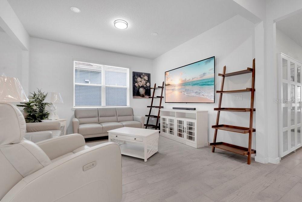 A living room features light gray flooring, a white sofa, a television, and a wooden ladder shelf — 1457 GRAND PALM DRIVE, ORLANDO, FL