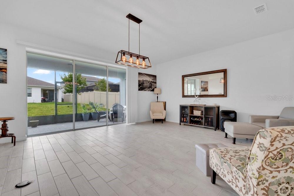 A bright living room features light tile flooring, a modern chandelier, and large sliding glass doors — 1457 GRAND PALM DRIVE, ORLANDO, FL