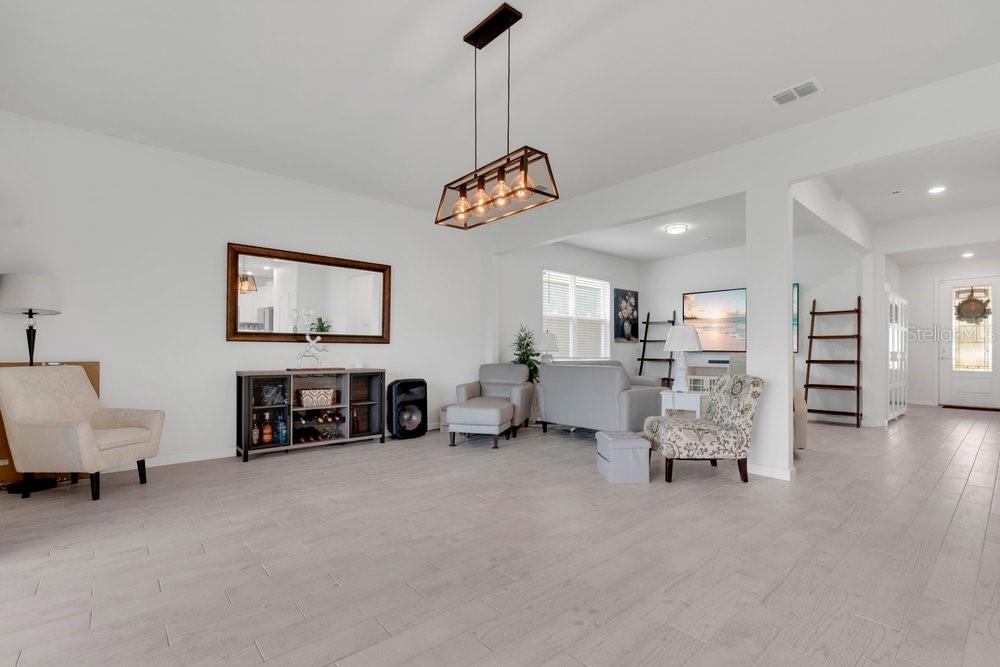 A bright, open-concept living room features light wood-look flooring, a modern chandelier, and neutral furniture — 1457 GRAND PALM DRIVE, ORLANDO, FL