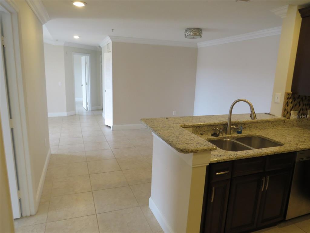 A kitchen with granite countertops and dark cabinets overlooks an open living area with tile — 1950 SUMMER CLUB DRIVE UNIT 306, OVIEDO, FL