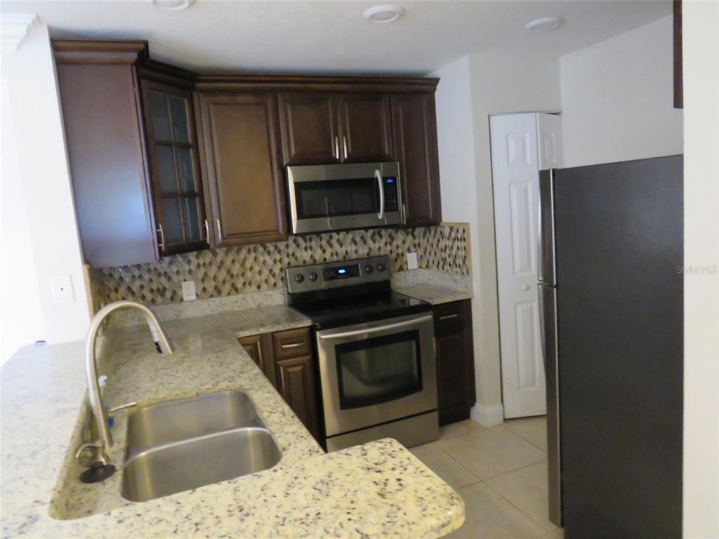 A kitchen features dark wood cabinets, granite countertops, stainless steel appliances, and a tiled backsplash — 1950 SUMMER CLUB DRIVE UNIT 306, OVIEDO, FL