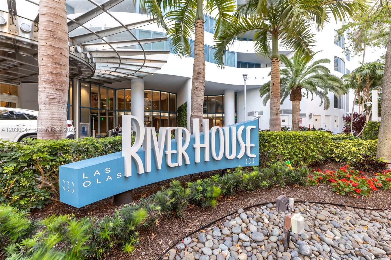 A blue sign for River House stands in front of a modern building with palm trees — FORT LAUDERDALE, FL