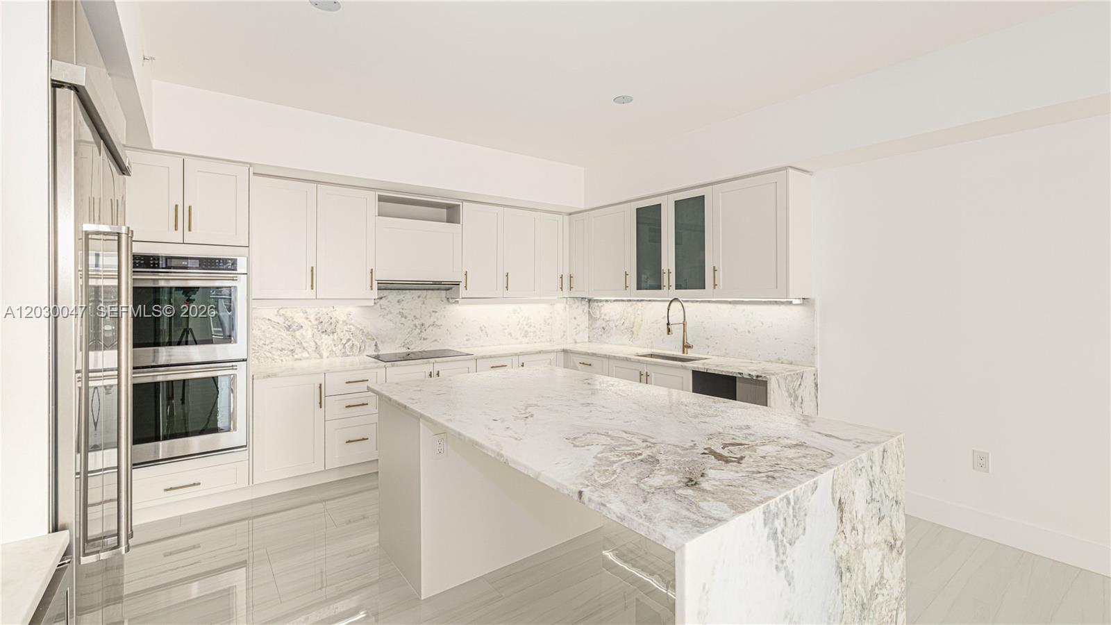 A modern kitchen features white cabinetry, marble countertops, a central island, and stainless steel appliances — FORT LAUDERDALE, FL