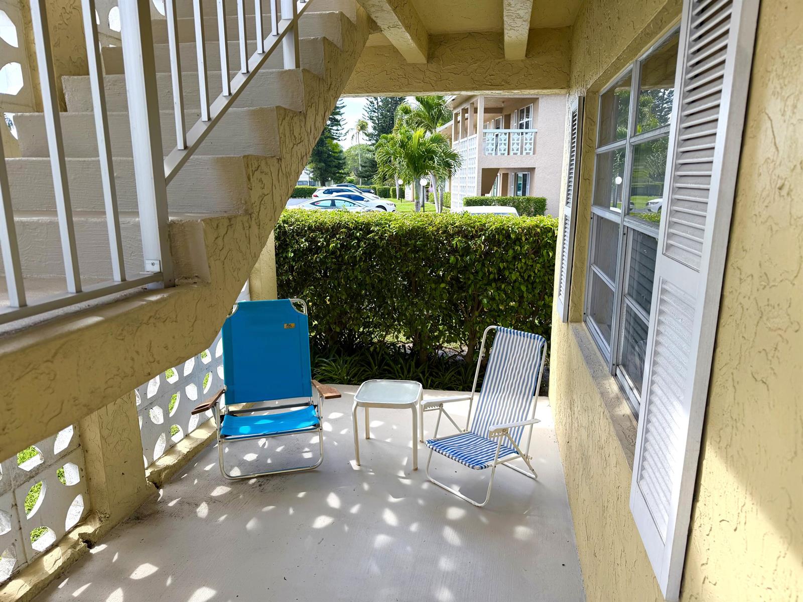 A covered patio features two folding chairs, a small table, and a staircase — 1141 Violet Terrace # 101, Delray Beach FL 33445, DELRAY BEACH, FL