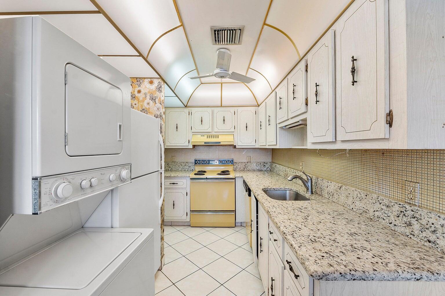 A galley kitchen features white cabinets, granite countertops, a yellow stove, and a stacked laundry unit — 1141 Violet Terrace # 101, Delray Beach FL 33445, DELRAY BEACH, FL