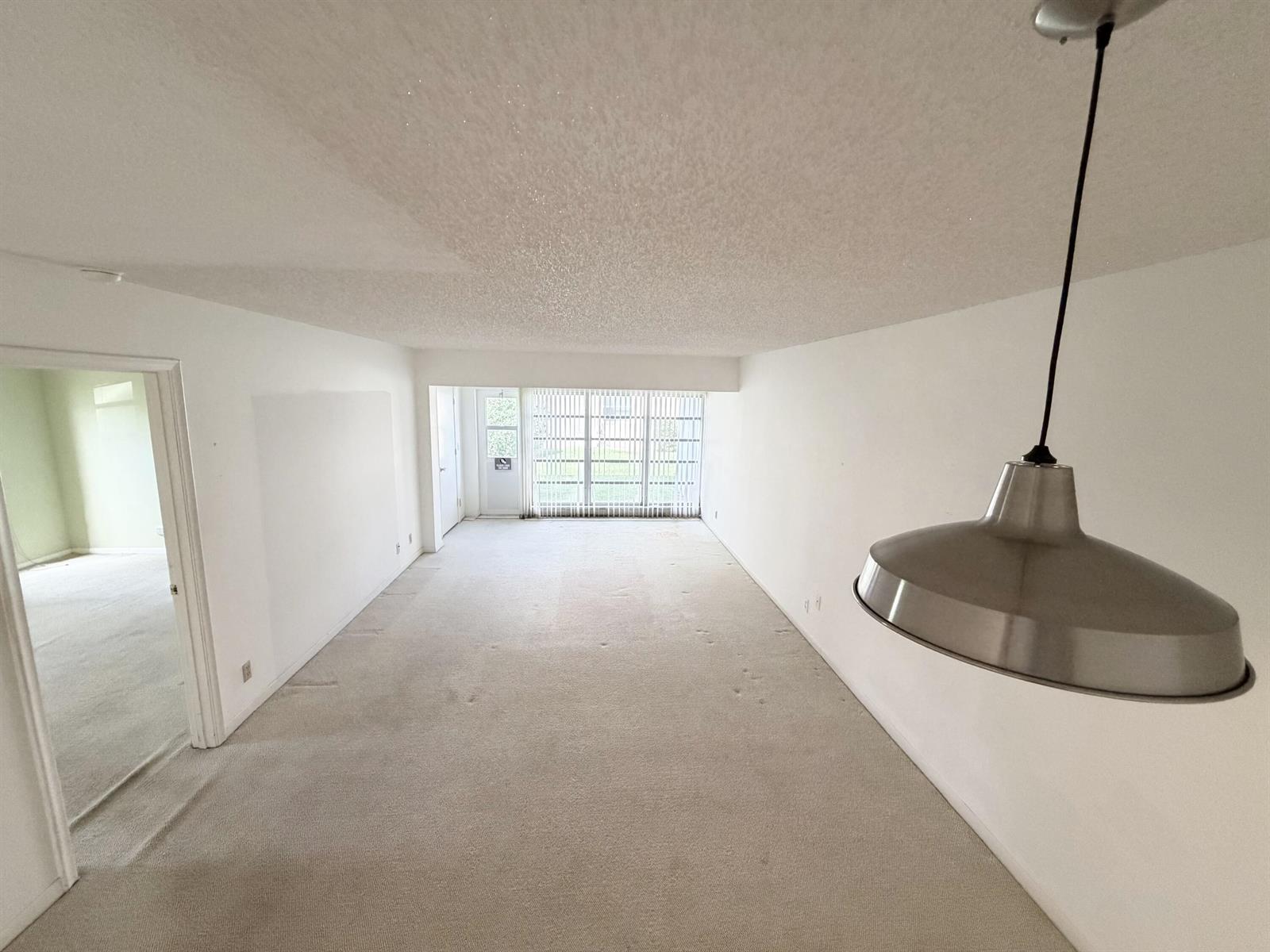 An empty living room features beige carpeting, white walls, a pendant light, and sliding doors — 1141 Violet Terrace # 101, Delray Beach FL 33445, DELRAY BEACH, FL