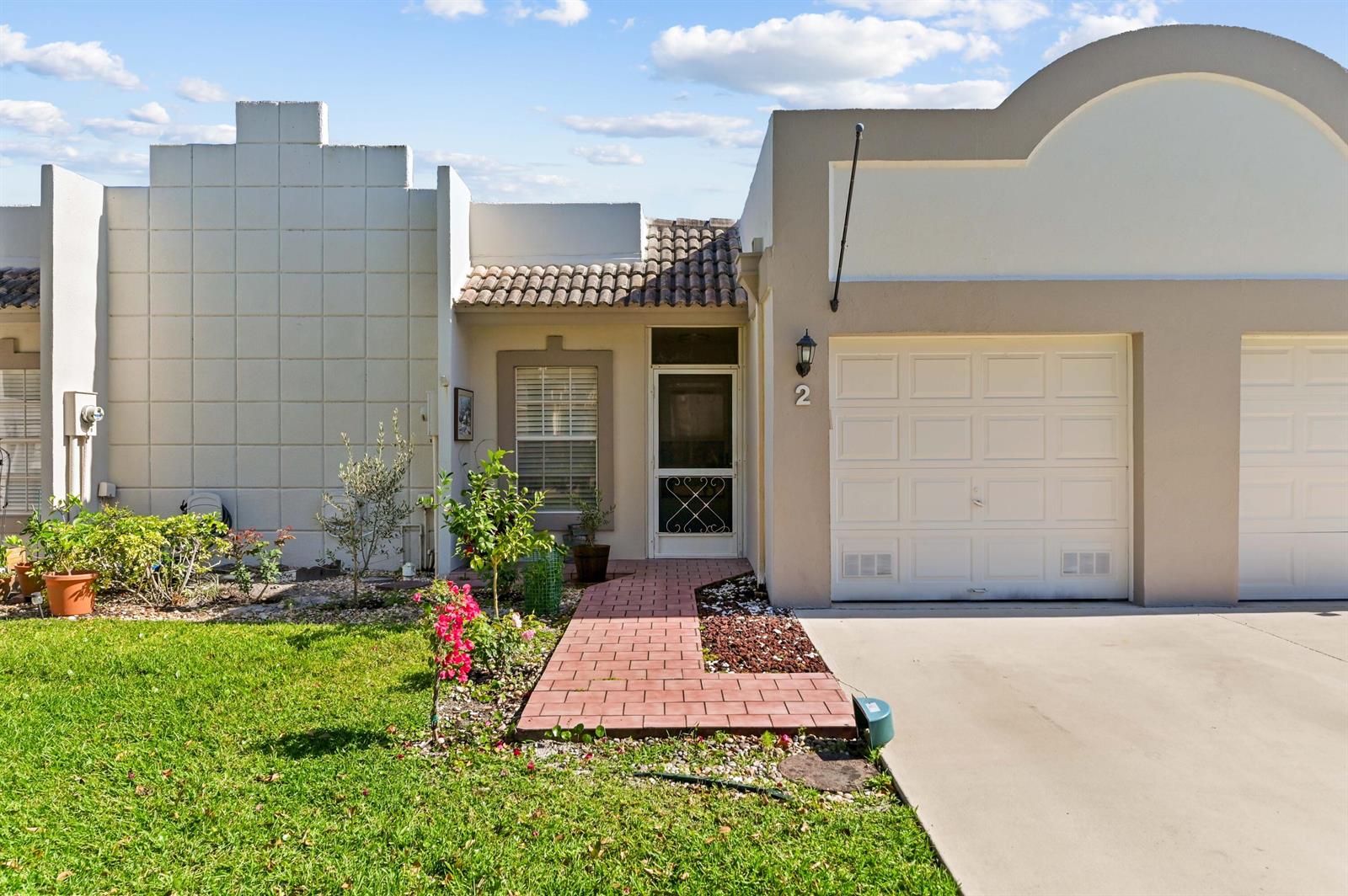 A single-story townhouse with a white garage, brick walkway, and a small front garden — 9244 Flynn Circle # 2, Boca Raton FL 33496, BOCA RATON, FL