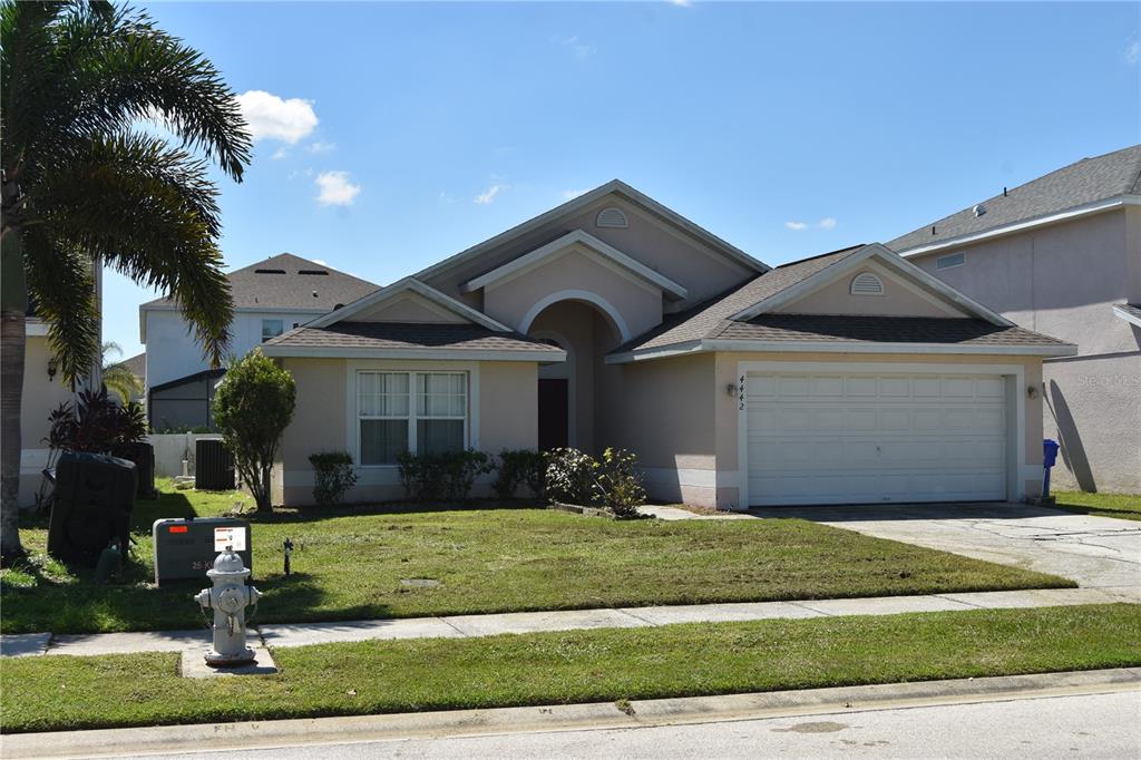 A single-story suburban house with a tan exterior, a two-car garage, and a front lawn — 4442 GREAT HARBOR LANE, KISSIMMEE, FL