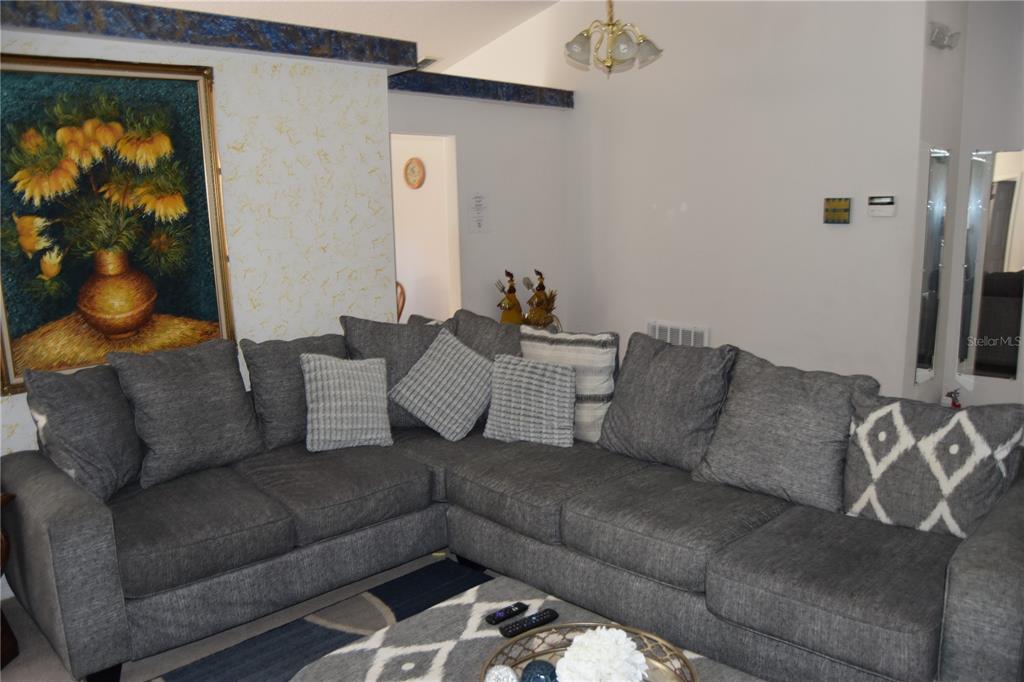 A living room features a large gray sectional sofa, a patterned rug, and wall art — 4442 GREAT HARBOR LANE, KISSIMMEE, FL