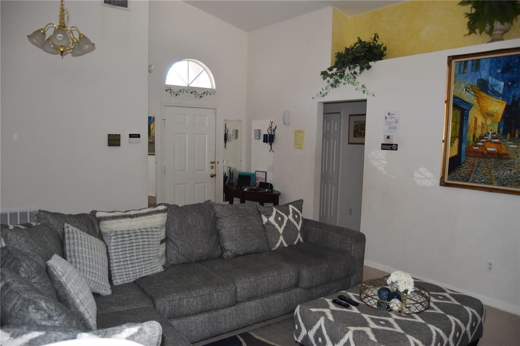 A living room features a gray sectional sofa, a patterned ottoman, and high vaulted ceilings — 4442 GREAT HARBOR LANE, KISSIMMEE, FL