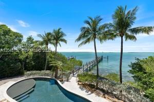A swimming pool overlooks a wooden pier extending into the ocean with palm trees nearby — 104 Coastal Dr, Key Largo FL 33037, KEY LARGO, FL