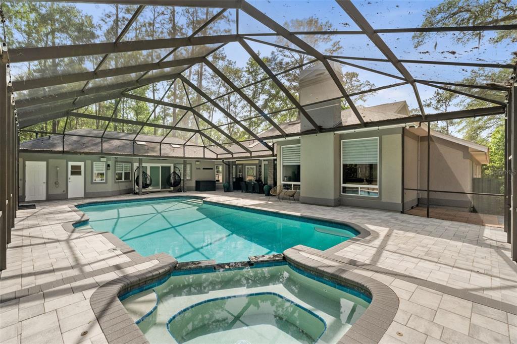 A screened-in patio features a swimming pool, a hot tub, and light-colored stone pavers — 8701 SW 46TH LANE, GAINESVILLE, FL