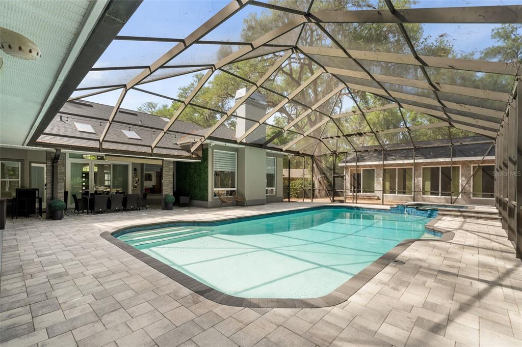 A screened-in patio features a swimming pool, a hot tub, and stone paver flooring — 8701 SW 46TH LANE, GAINESVILLE, FL