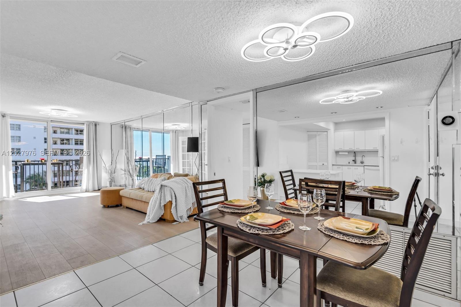 A dining area with a wooden table and chairs sits before a mirrored wall — 9273 Collins Ave # 503, Surfside FL 33154, SURFSIDE, FL